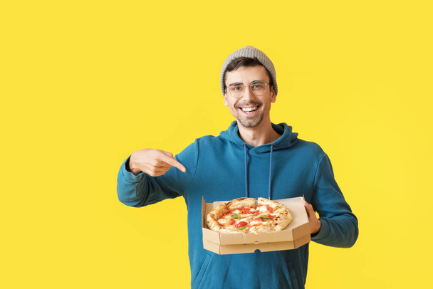 Yakışıklı adam arka planda lezzetli pizzaya işaret ediyor. - Fotoğraf, Görsel