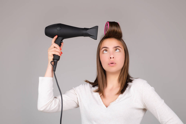 Woman with hair dryer. Funny girl with straight hair drying hair with professional hairdryer. Hairstyle, hairdressing concept. - Фото, зображення
