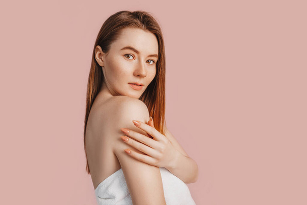 Beautiful sensual young girl with clean skin on a pink background with a mockup. Topless woman in a towel. The concept of spa treatments, natural beauty and care, youth, cream and mask, freshness - Foto, afbeelding