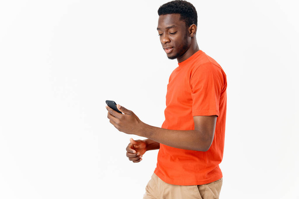 handsome african man with mobile phone on light background and orange t-shirt shorts - Fotografie, Obrázek