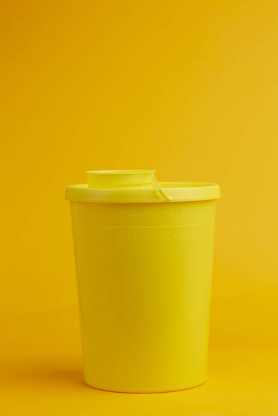 Front view of container with round cap on seamless yellow background for the disposal of used injector needles with drug residue. - Fotó, kép