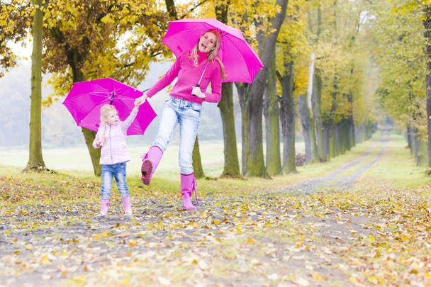 μητέρα και κόρη με ομπρέλες σε φθινοπωρινό δρομάκι - Φωτογραφία, εικόνα
