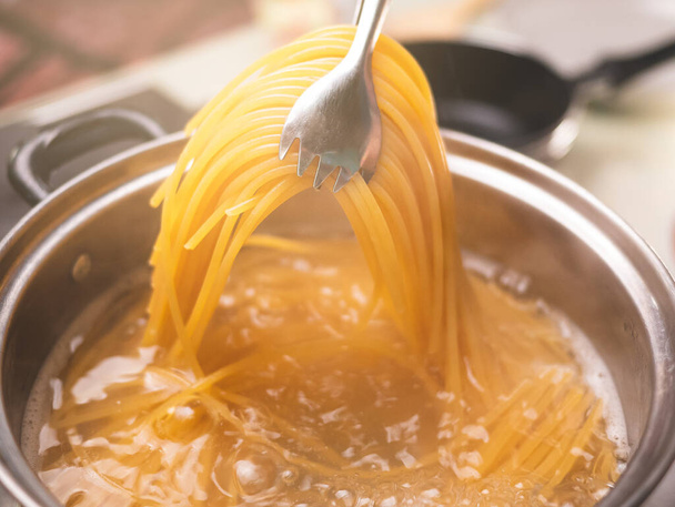 Raw spaghetti is being cooked in boiling water in a kitchen pot. Healthy Italian Food and Cooking concepts. - Foto, Imagen