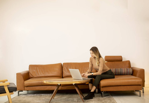 Fiatal gyönyörű nő használja a laptop a kanapén otthon - Fotó, kép