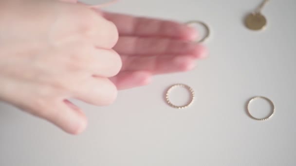 Jonge vrouw handen nemen gouden ketting met witte edelsteen uit onder ringen en sieraden op witte tafel extreme closeup. - Video