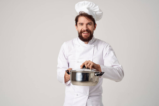 Vrolijke mannelijke chef-kok met een steelpan in zijn handen smaakt food professional - Foto, afbeelding