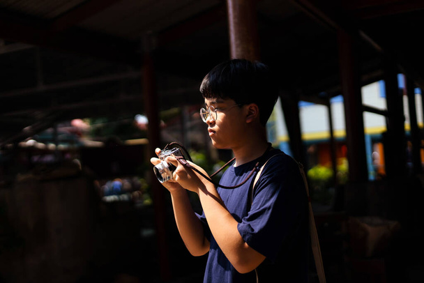 Asian teenage boys holds a vintage film camera and take pictures at tourist attractions. - Zdjęcie, obraz