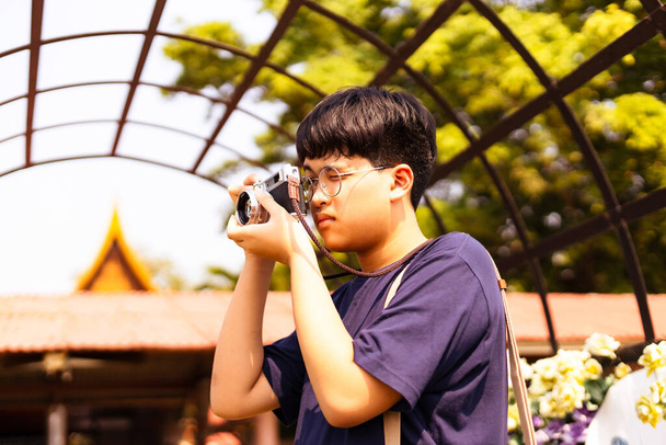 アジアの十代の男の子はヴィンテージフィルムカメラを保持し、観光スポットで写真を撮る. - 写真・画像