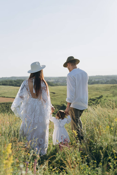 Happy young family spending  time together in nature, beautiful woman in white guipure dress with husband and their daughter walking  in the field - Fotoğraf, Görsel