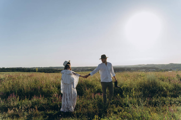 Happy young family spending  time together in nature, beautiful woman in white guipure dress holding her daughter and walking with husband in the field - Foto, Bild