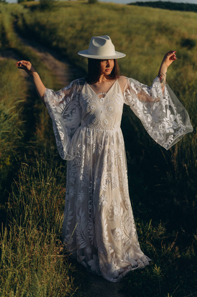 The beautiful woman in white guipure dress and in hat posing in the field - Photo, Image