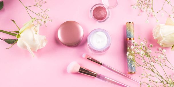 Trendy make-up borstels met producten op roze achtergrond met gypsophila bloemen - Foto, afbeelding