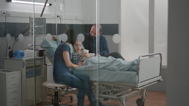 Besorgte Eltern sitzen mit kranker Tochter und warten auf Krankheits-Expertise bei ärztlicher Untersuchung - Foto, Bild