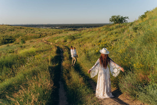 Happy young family spending  time together in nature, the man holding his daughter and walking with his beautiful wife in the field - Fotoğraf, Görsel