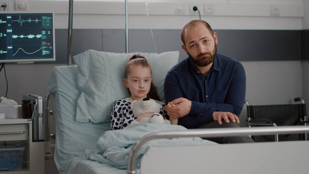 Endişeli baba portresi hastanede hasta kız elini tutuyor kameraya bakıyor. - Fotoğraf, Görsel