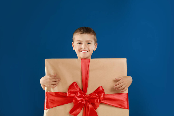 Aranyos kisfiú, ajándékdoboznak öltözve, kék háttérrel. Karácsonyi öltöny - Fotó, kép