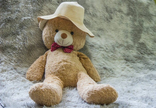 Большой коричневый плюшевый медведь в шляпе сидит на шерстяной ткани. - Фото, изображение