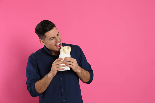 Człowiek jedzący pyszne shawarma na różowym tle, miejsce na tekst - Zdjęcie, obraz