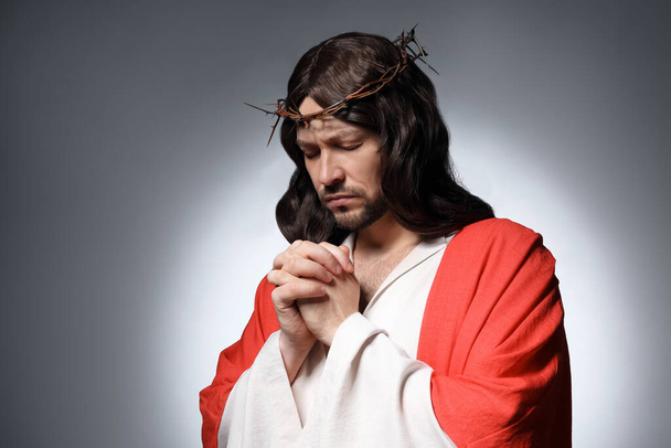 Jesus Christ with crown of thorns praying on grey background - Photo, Image