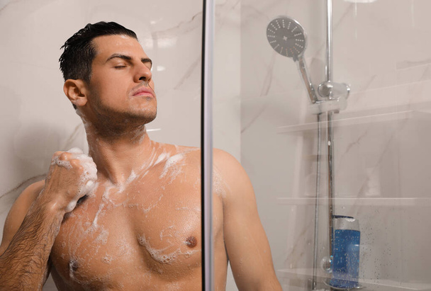 Handsome man with sponge taking shower at home - Valokuva, kuva