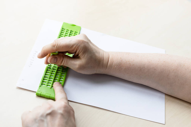 θηλυκό χέρι εκτυπώνει λέξεις σε braille με σχιστόλιθο και γραφίδα από κοντά - Φωτογραφία, εικόνα