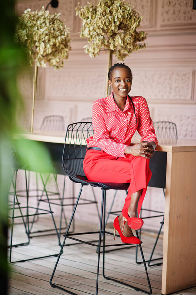 きれいな編組ビジネスアフリカ系アメリカ人女性明るい胸の人フレンドリーな着用オフィス赤いシャツとズボン,椅子に座って. - 写真・画像