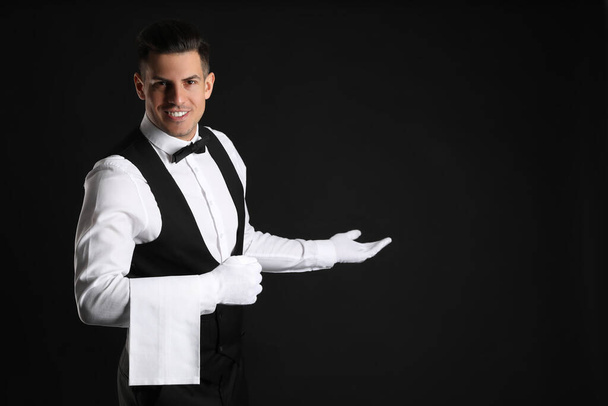 Handsome butler with towel on black background, space for text - Фото, изображение