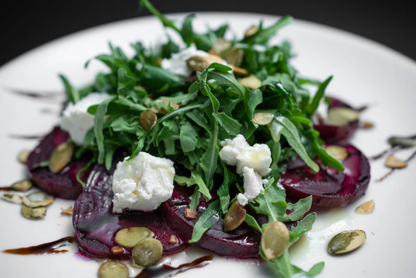 closeup of salad with beet, arugula and feta cheese on plate on black background - Zdjęcie, obraz