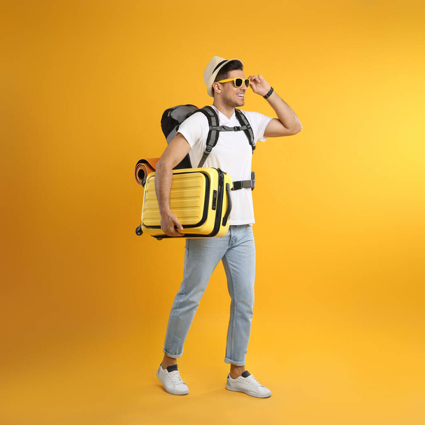 Male tourist with travel backpack and suitcase on yellow background - Photo, Image