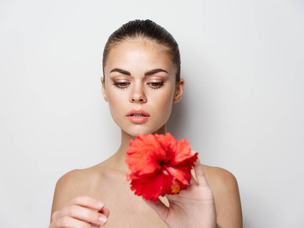 mujer sosteniendo una flor roja en su mano sobre un fondo claro  - Foto, Imagen