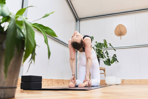 Mulher branca esticando as costas, formando um arco para realizar uma pose de ioga complicada - Foto, Imagem
