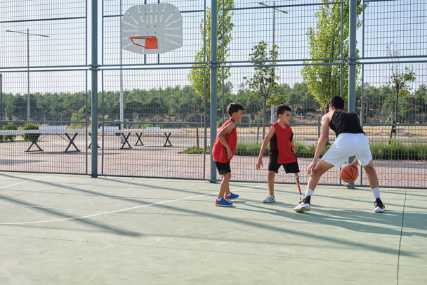 Tres hermanos jugando baloncesto, uno de ellos tiene una prótesis de pierna. Hermanos jugando al basket. - Foto, Imagen