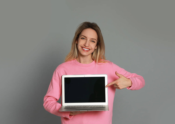Young woman with modern laptop on grey background - 写真・画像