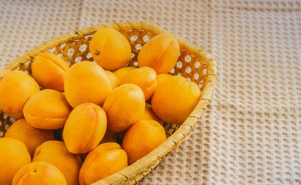 Juicy ripe apricots in a wicker basket on a towel. - Фото, зображення