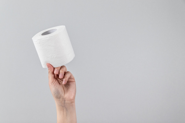 La mano femenina sostiene un rollo suave de papel higiénico sobre un fondo gris con espacio para copiar. Composición mínima para publicidad, artículo - Foto, imagen