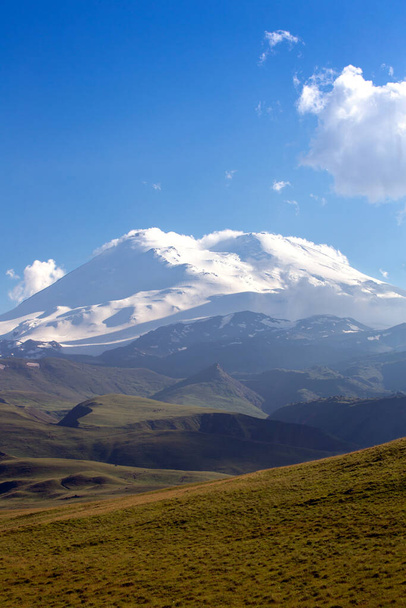 Lumihuippuiset vuorenhuiput kesäpäivänä. Elbrus taustalla vihreitä kukkuloita. Vuoristomaisema. Kaukasuksen vuoret. Sininen taivas pilvillä. Venäjän luonne. - Valokuva, kuva