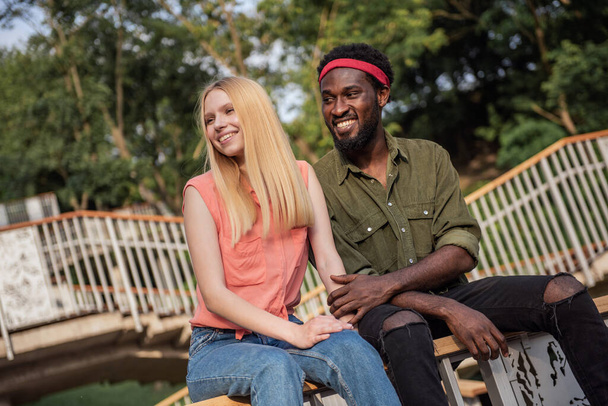 Young cheerful couple where a dark-skinned man and a blonde woman are smiling holding each other's hands while walking down a city street - Foto, Bild