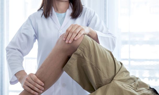 Médico femenino manos haciendo fisioterapia Al extender la pierna y la rodilla de un paciente masculino. - Foto, imagen
