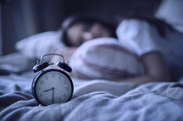 Junge Frau ruht sich in ihrem Bett aus, Mitternachtszeit auf dem Wecker, Nachträume - Foto, Bild