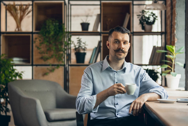 One young smiling businessman, office worker sitting on chair with cup of coffee. Business, working process concept. - Valokuva, kuva