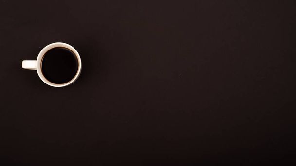 Top view of white ceramic mug with black coffee on black background. Copy space - Фото, изображение