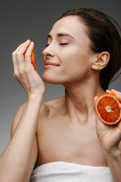 White brunette woman smiling while smelling grapefruit isolated over grey background - Photo, image