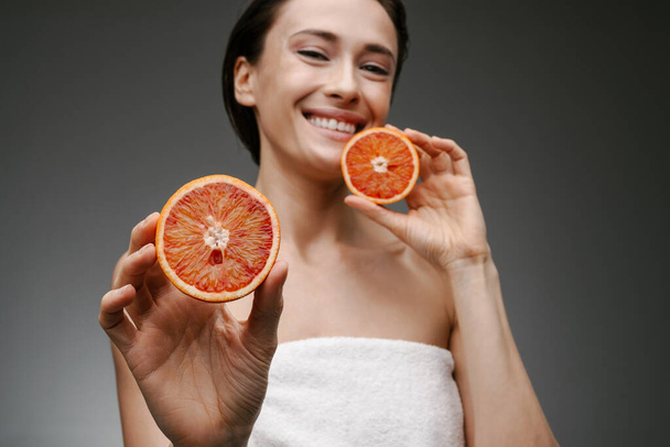 Smiling healthy mid aged topless woman holding grapefruit over gray wall background - Photo, image