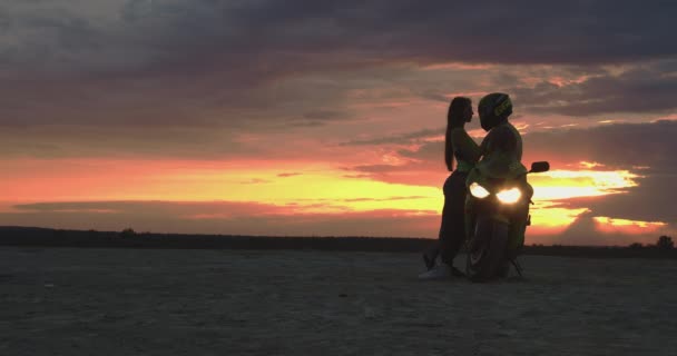 Пара обнимается возле мотоцикла на пляже на закате - Кадры, видео