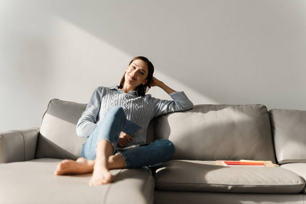 Young smiling woman holding planner while sitting on sofa at home - Foto, Bild