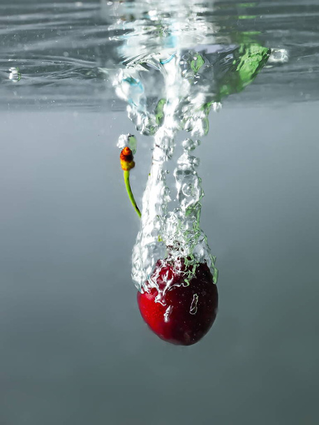 ripe cherries fall into the water raising splashes and air bubbles - Photo, image