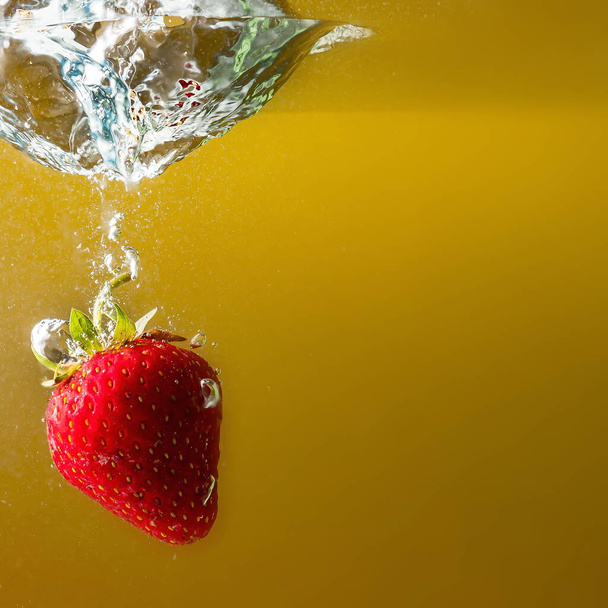 ripe strawberries fall into the water lifting splashes and air bubbles - Photo, image