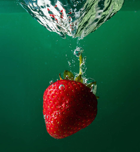 спелые клубники падают в воду, поднимая брызги и пузыри воздуха - Фото, изображение