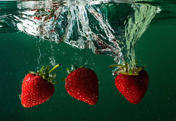 ripe strawberries fall into the water lifting splashes and air bubbles - Foto, Imagem