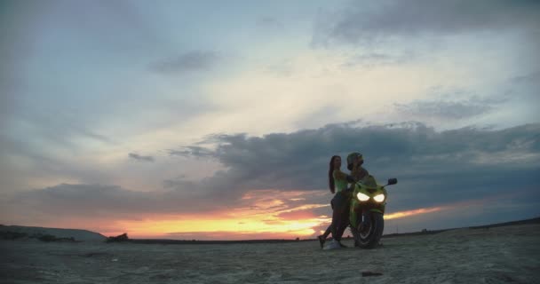 Пара обнимается возле мотоцикла на пляже на закате - Кадры, видео